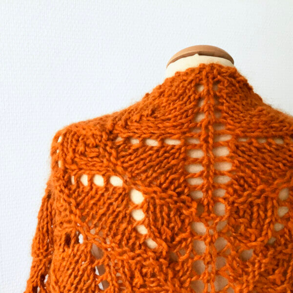 Atomic Tangerine: a close up of a bright orange bulky weight knit lace shawl, shown from the back on a mannequin against a white background.